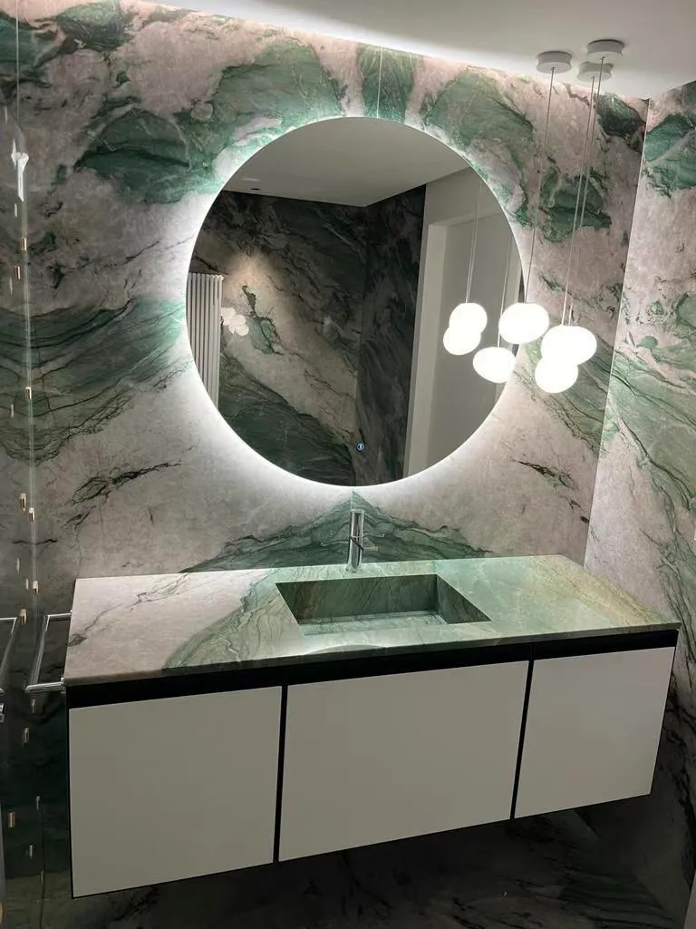 Bathroom clad in green natural stone, with a stone vanity and backlit mirror